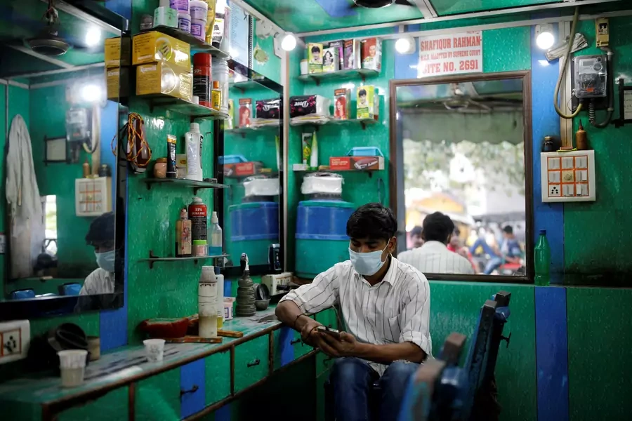 A barber wearing a protective face mask looks at his mobile phone.