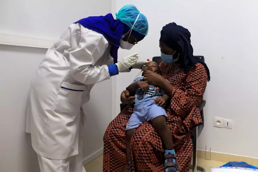 A healthcare worker wearing protective gear takes a swab sample from a boy to test him for the coronavirus disease (COVID-19) at an Institute for Health Research, Epidemiological Surveillance and Training (IRESSEF) testing center, in Dakar, Senegal