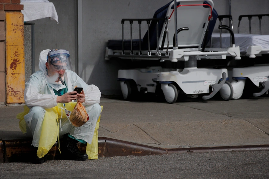 A healthcare worker sits on the curb as he uses a vaping device while taking a break outside Maimonides Medical Center.