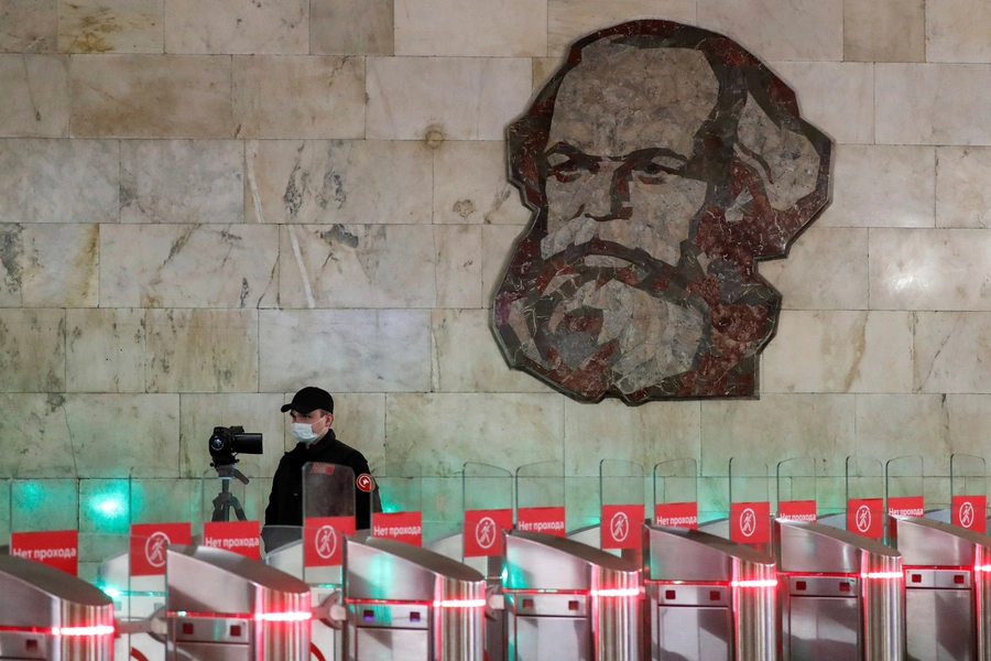 An employee wearing a protective mask uses a device to take passengers' body temperature near a mosaic artwork, which depicts German philosopher Karl Marx, at an entrance to a metro station in central Moscow.