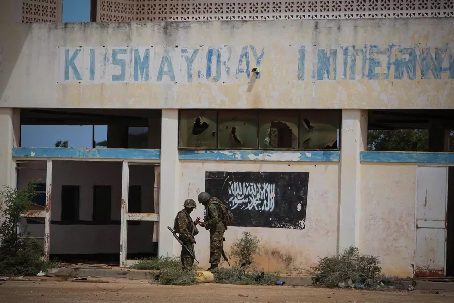 Soldiers of the Kenyan Contingent serving with the African Union Mission in Somalia (AMISOM) stand in front of the black flag of the al Qaeda-affiliated extremist group Al Shabab painted on the wall of Kismayo Airport on October 2, 2012.