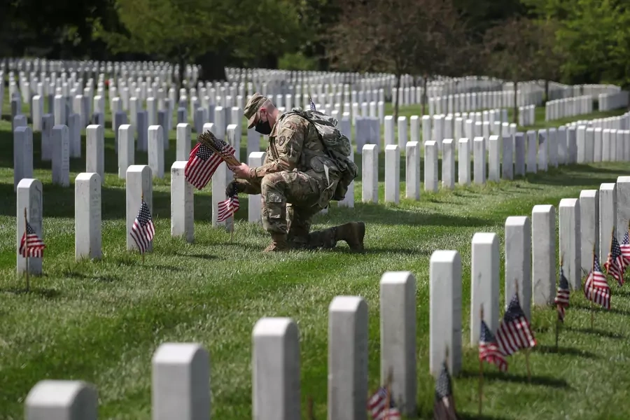 A member of the U.S. Army Old Guard places American flags near headstones at Arlington National Cemetery on May 21, 2020.