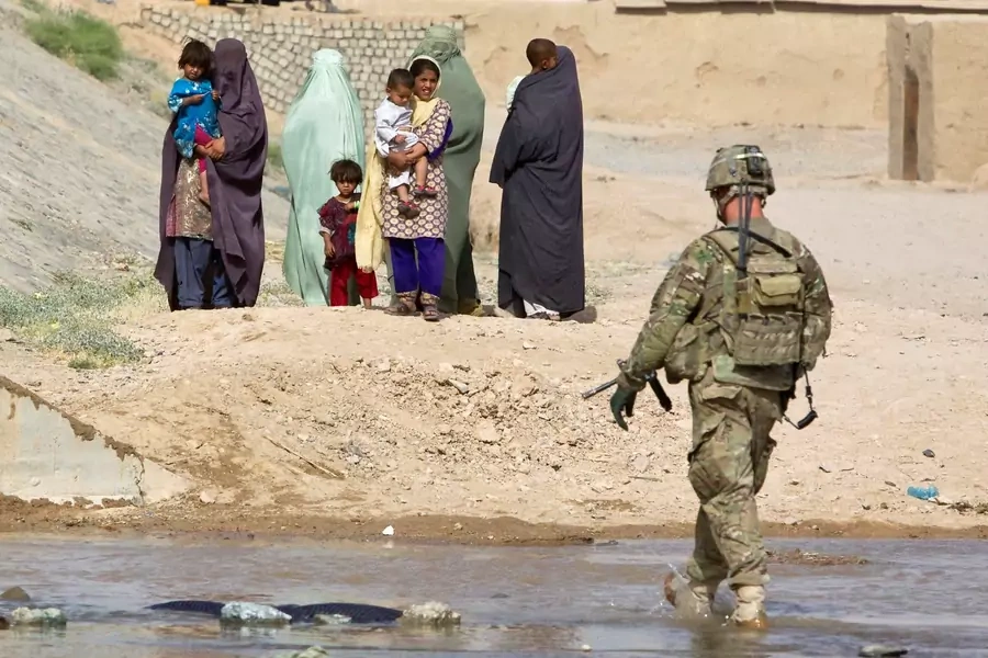 A U.S. Army soldier walks toward Afghan women with children.