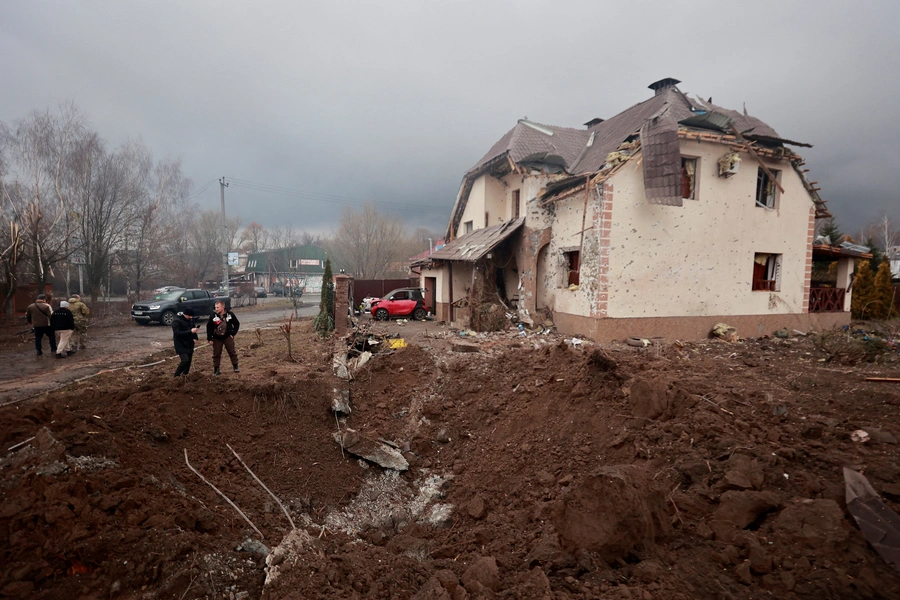 People stand next to a shell crater in front of a house damaged by recent shelling in the village of Hatne, in the Kyiv region, on March 3, 2022. 