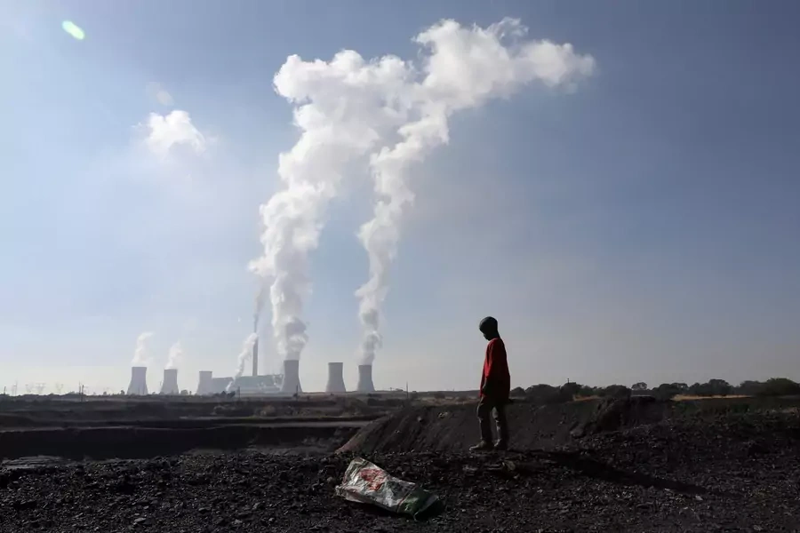 A child collecting chunks of coal looks on at a colliery while smoke rises from the Duvha coal-based power station owned by state power utility Eskom, in Emalahleni, Mpumalanga province, South Africa on June 2, 2021.