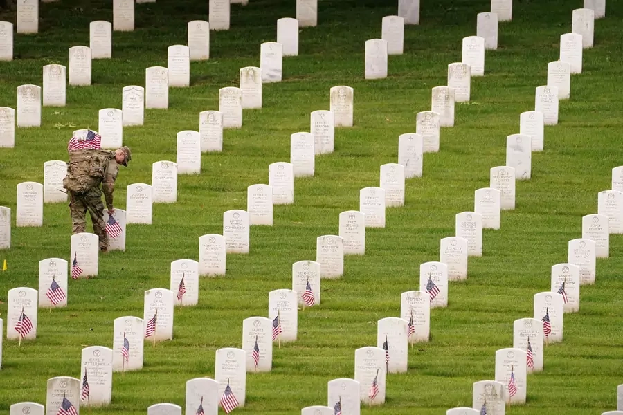 A soldier of the 3rd U.S. Infantry Regiment places flags on headstones in Arlington National Cemetery ahead of Memorial Day on May 26, 2022. 