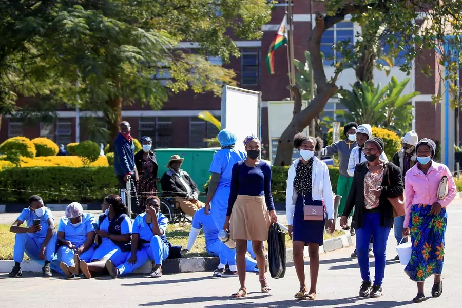 People walk past Zimbabwean medical workers as they sit outside Sally Mugabe Hospital during a strike by state doctors and nurses for higher pay, in Harare, Zimbabwe, June 20, 2022.