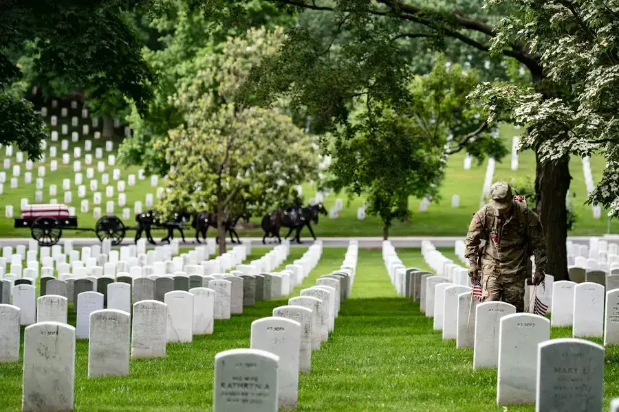 A soldier places a flag at a gravestone in Arlington National Cemetery as part of the annual pre-Memorial Day tradition called Flags In. May 26, 2022. 