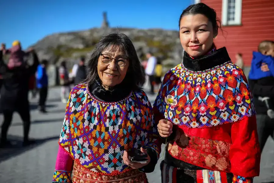 A young and an old woman in traditional Inuit clothing stand after a baptism in front of the Nuuk Cathedral (Church Of Our Saviour) in Nuuk, Greenland, September 5, 2021