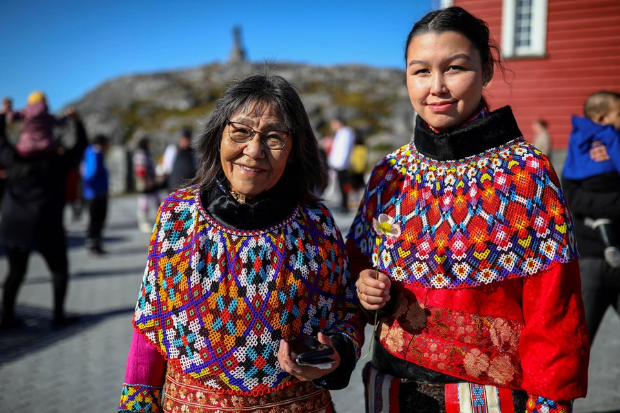 A young and an old woman in traditional Inuit clothing stand after a baptism in front of the Nuuk Cathedral (Church Of Our Saviour) in Nuuk, Greenland, September 5, 2021