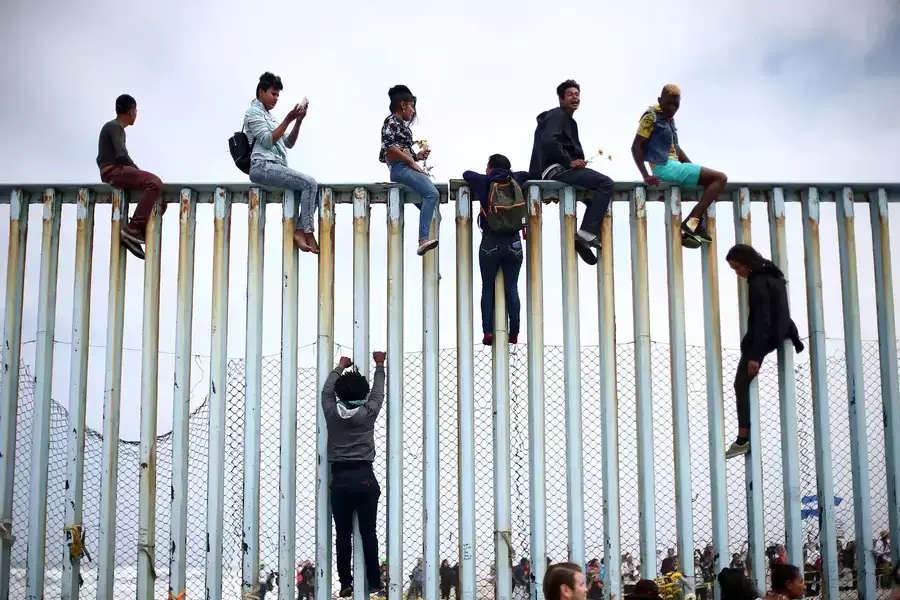 Migrants from Central America climb up the border fence between Mexico and the United States prior to an asylum request in the United States