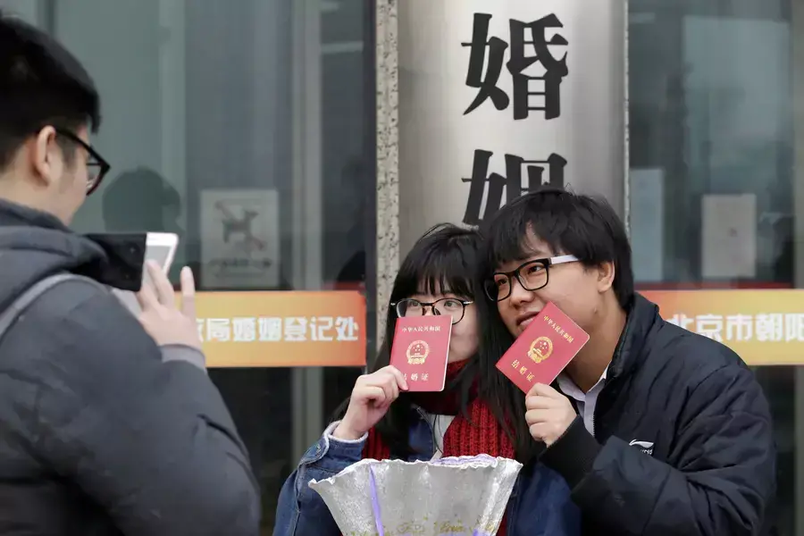 A couple holding marriage certificates poses for a photo outside a registry office of marriage in Beijing, China.