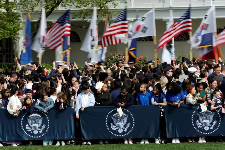 Military personnel carry U.S. and South Korean flags as people wait for an official state arrival ceremony for South Korean President Yoon Suk Yeol at the White House on April 26, 2023. 