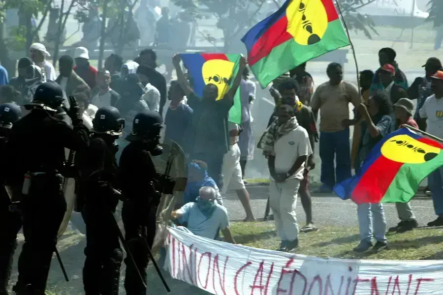 Pro-independance demonstrators hold a Kanak flags as they face French riot police during a protest outside the New Caledonian northern province assembly while French President Jacques Chirac was paying a visit to the New Caledonian northern city of Kone o
